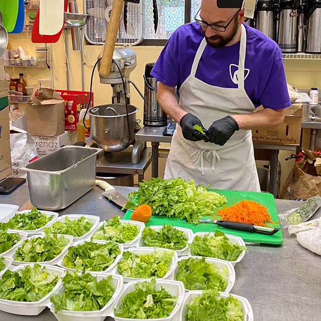 A man preps greens and carrots in a kitchen