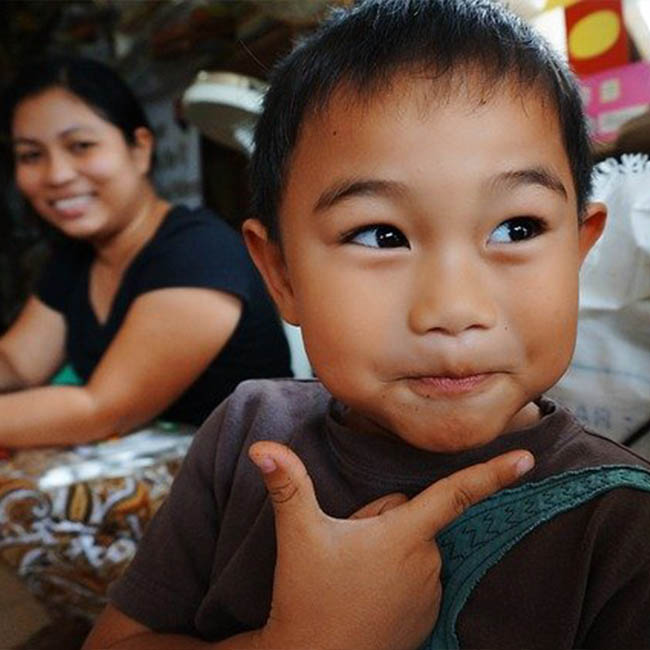 A young Pilipino boy smirks with his mother smiling behind him