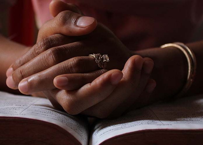 Hands folded in prayer on top of a Bible