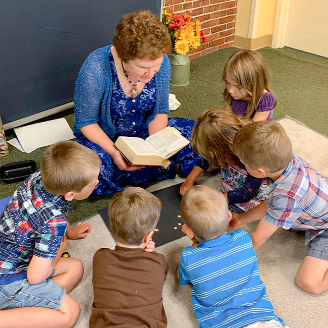A preschool Sunday school class gathers around their teacher while she reads from the Bible