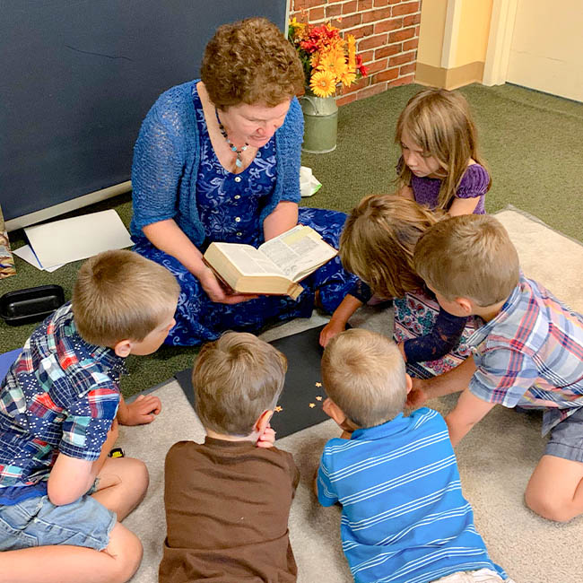 A preschool Sunday school class gathers around their teacher while she reads from the Bible