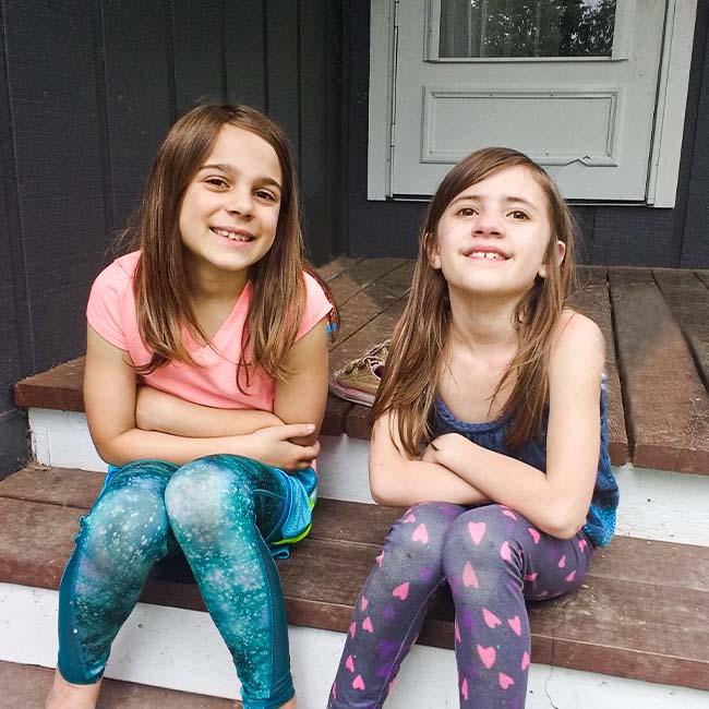Two elementary-age friend sitting on a wooden step together smiling