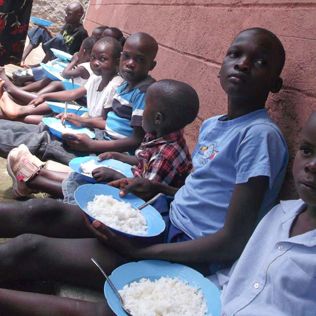 Ten children in Africa sitting outside a building eating rice