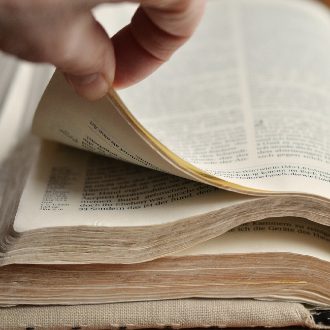 Two finger turning the pages of an open Bible