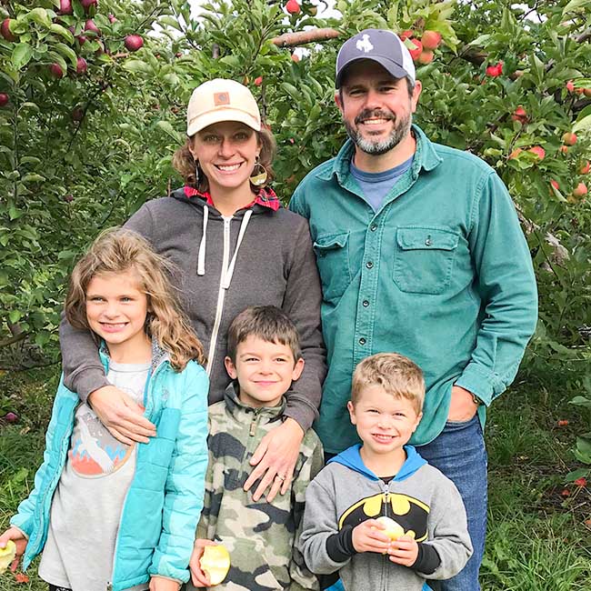 Ben, his wife and three children smiling for the camera in an apple orchard
